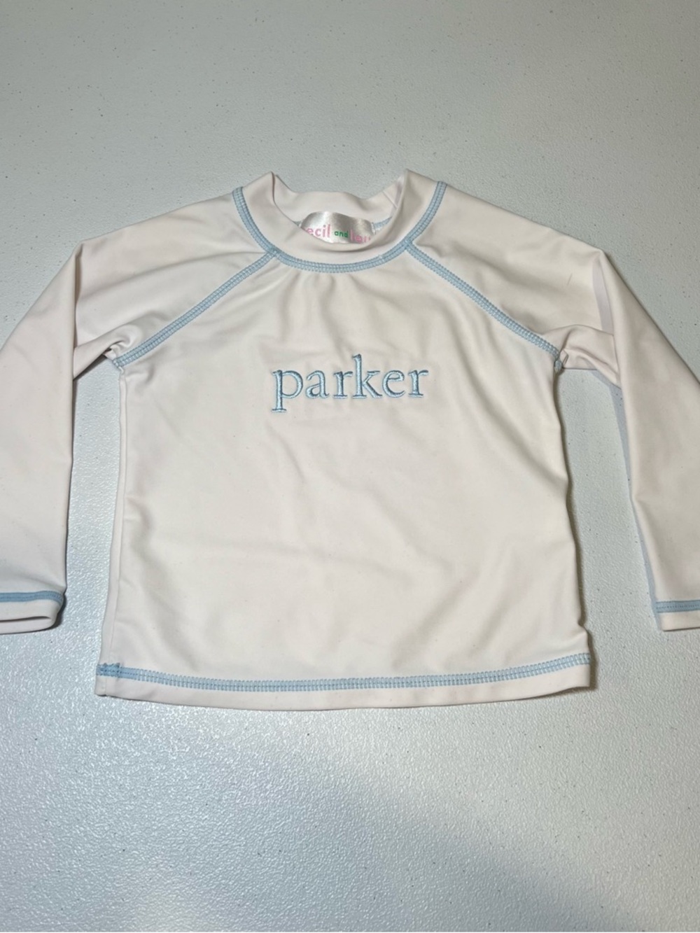 Cecil and Lou Kids White Rash Guard with Light Blue Trim and 'Parker' Embroidery